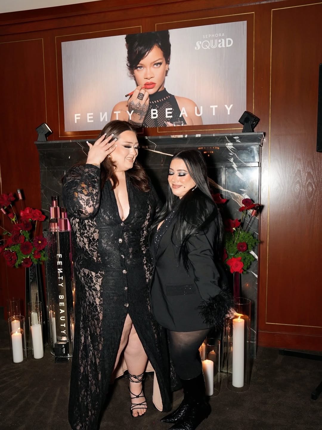 Two women posing in front of a Fenty Beauty display with a large poster in the background.