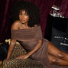 Woman in a brown off-shoulder dress sitting on a leopard print bench with a Fenty Beauty x Douglas background.