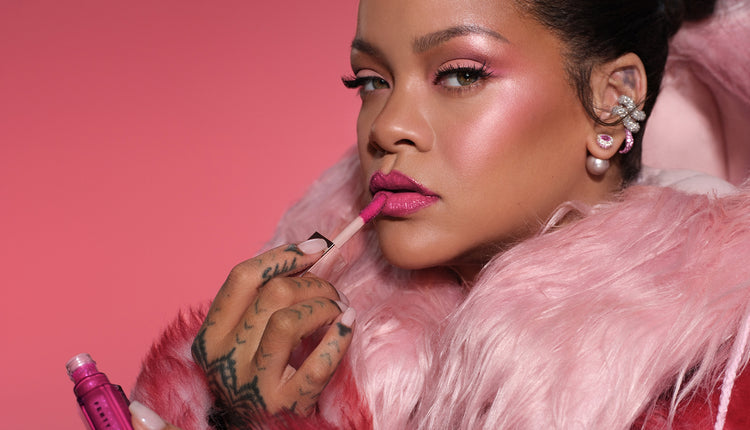 Rihanna applying pink lipstick against a pink background
